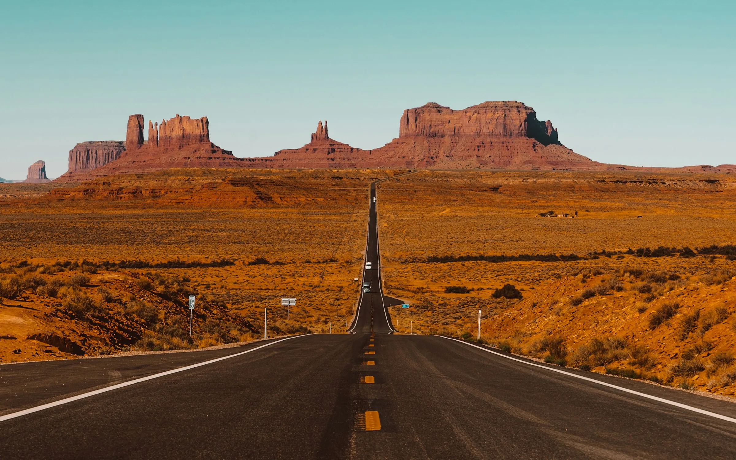 Estrada reta atravessando Monument Valley, com as formações de rocha vermelha no horizonte