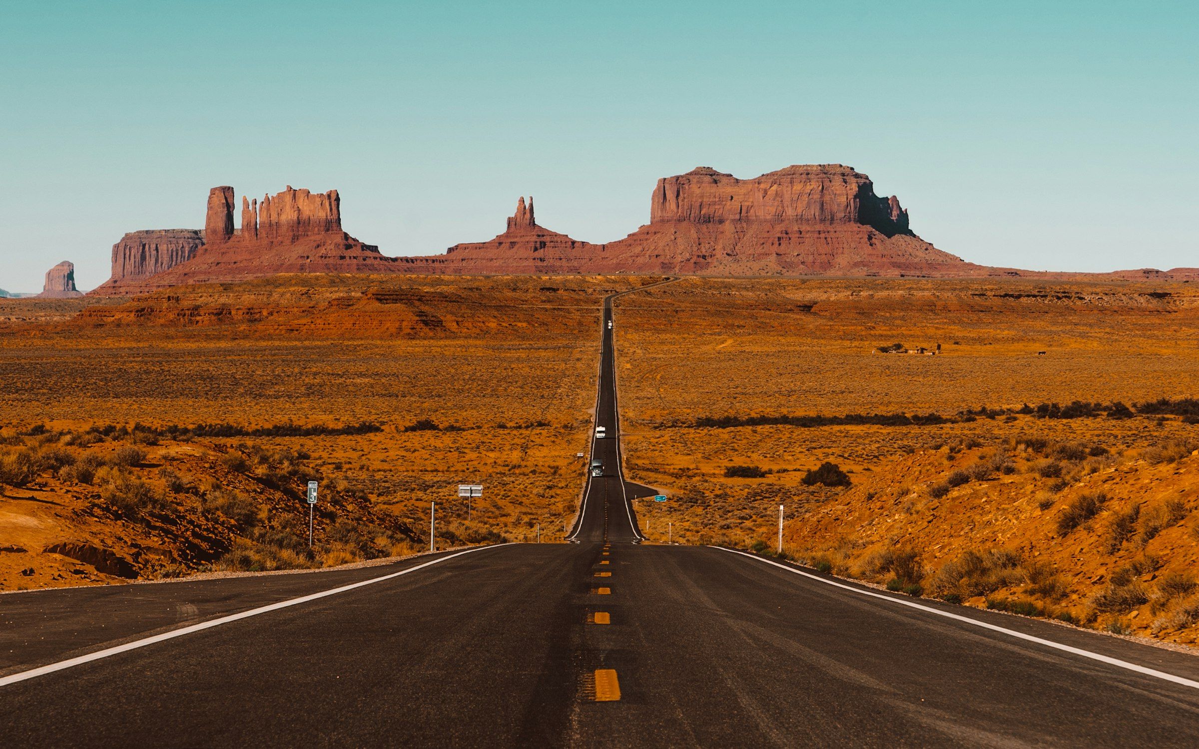 Estrada reta atravessando Monument Valley, com as formações de rocha vermelha no horizonte