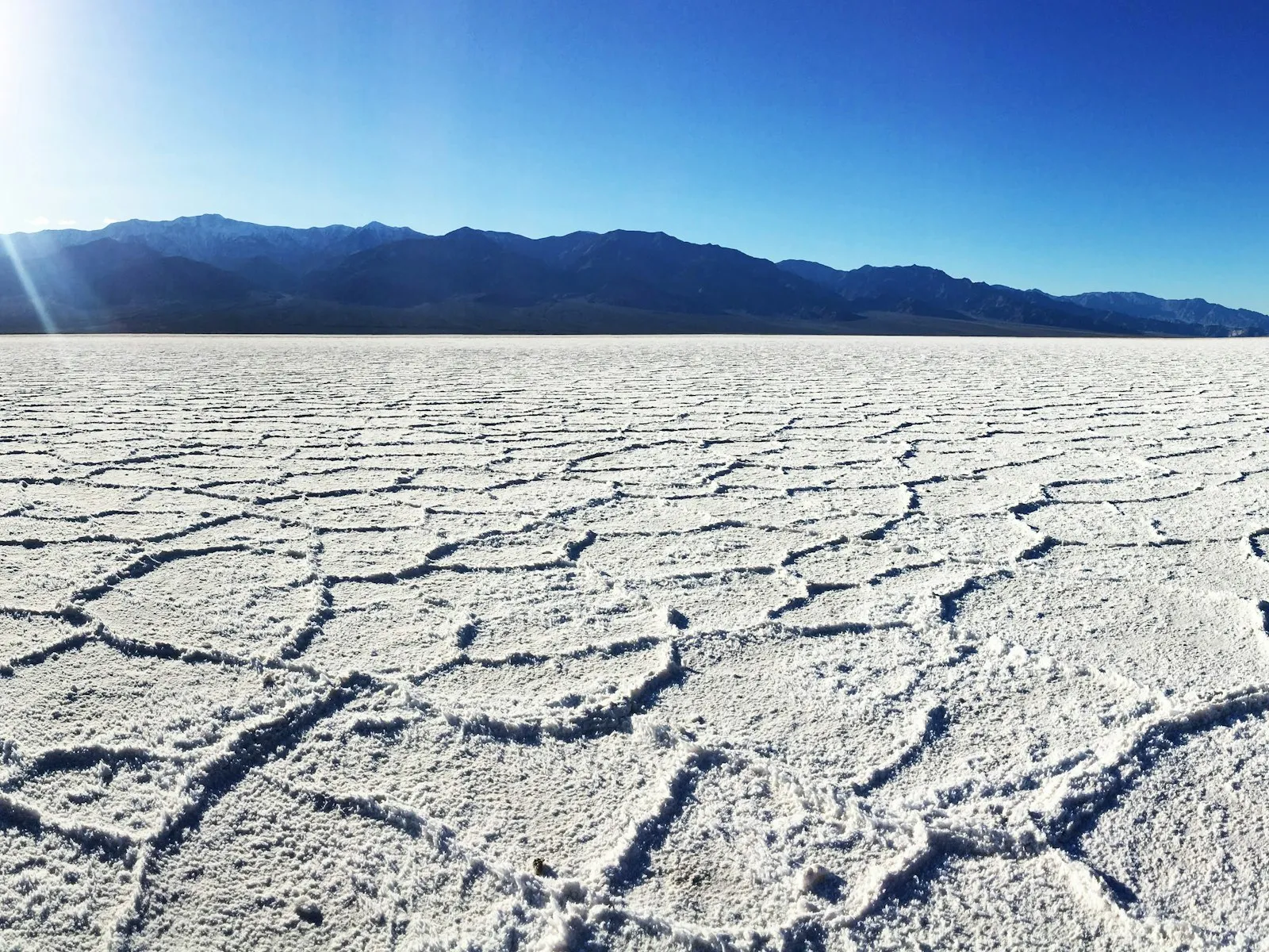 Crosta de sal em polígonos na bacia de Badwater, com montanhas escuras ao fundo e céu azul