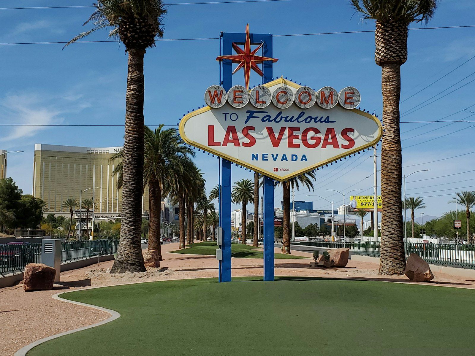 Placa "Welcome to Fabulous Las Vegas" entre palmeiras, sob céu azul, com hotéis ao fundo