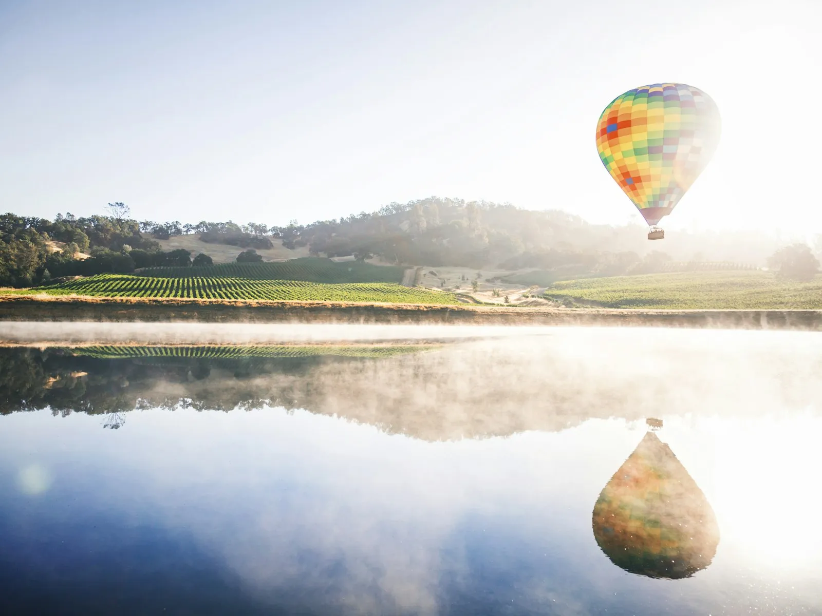 Balão de ar quente colorido sobre um lago no Napa Valley, refletido na água calma do amanhecer