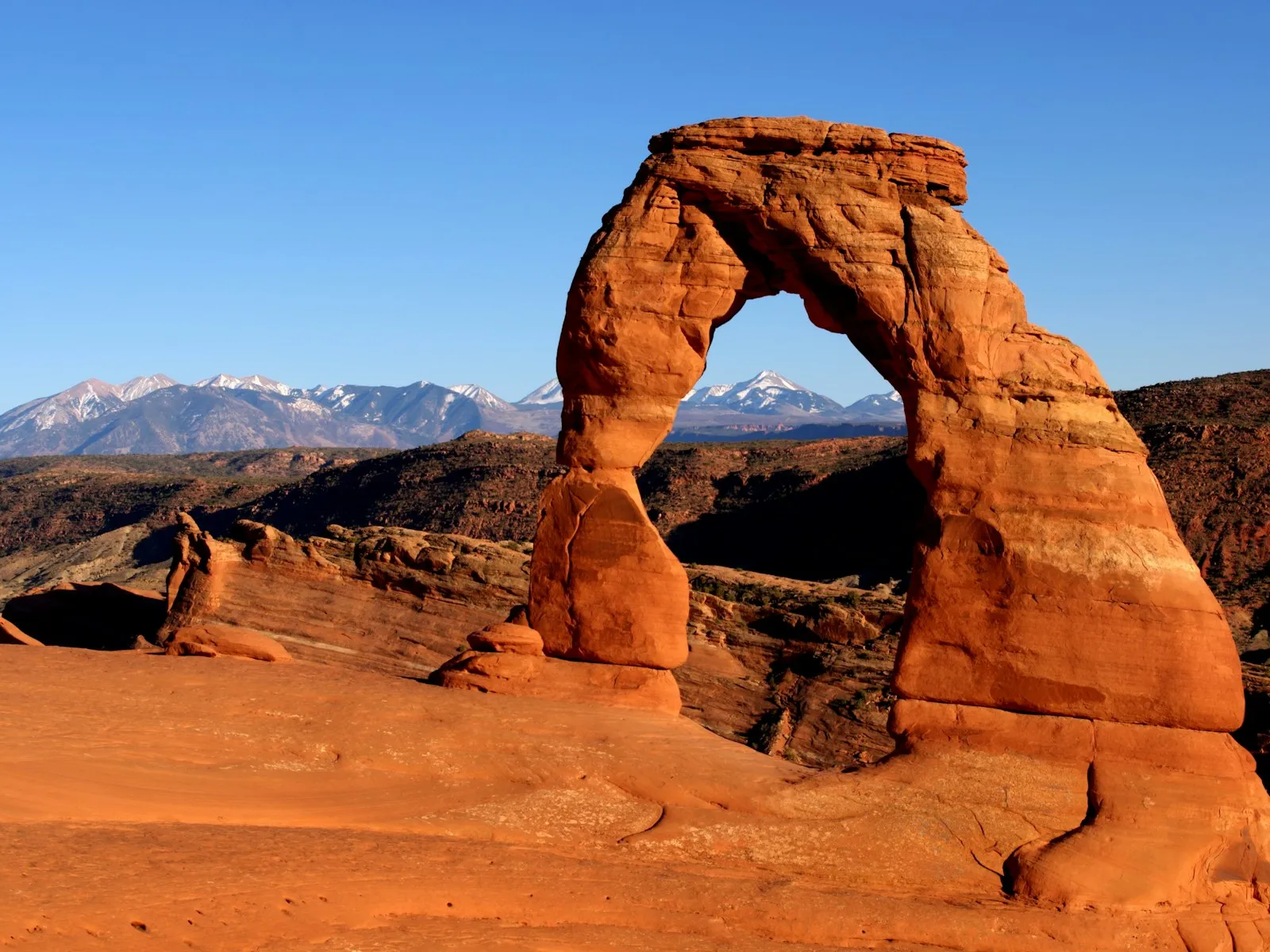 Delicate Arch, no Arches National Park, com as montanhas La Sal nevadas ao fundo e céu azul