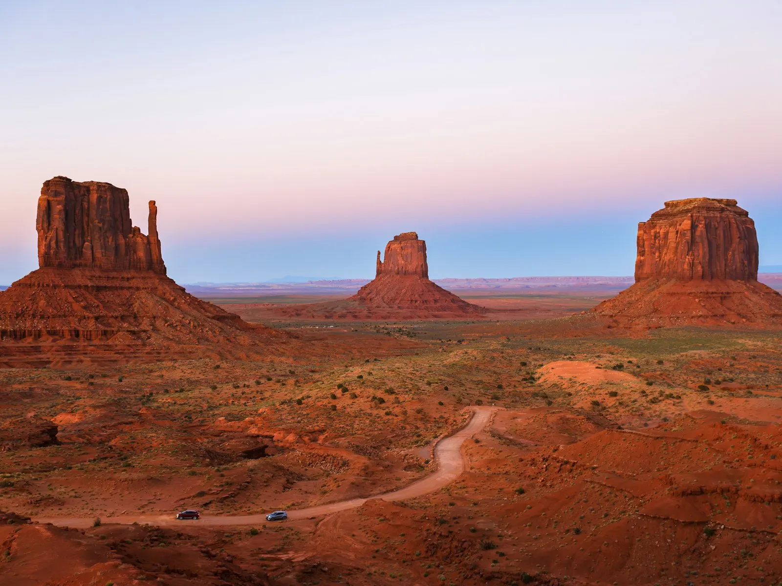 Monument Valley ao entardecer: as formações Mittens e Merrick Butte sobre o deserto vermelho, com uma estrada de terra